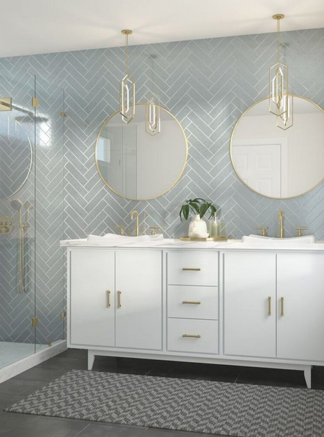 Bathroom with a white vanity, two round mirrors, and blue herringbone tile, with gold fixtures.