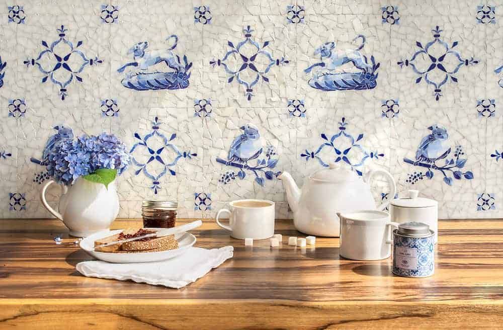 A table set for tea with toast, jam, and flowers against blue and white patterned tile.