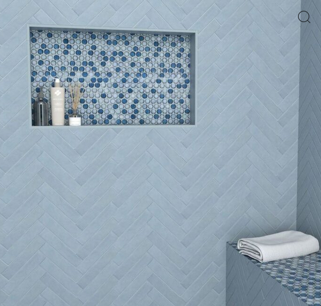 Blue tiled shower with a built-in shelf of patterned tiles and a bench with a folded towel.