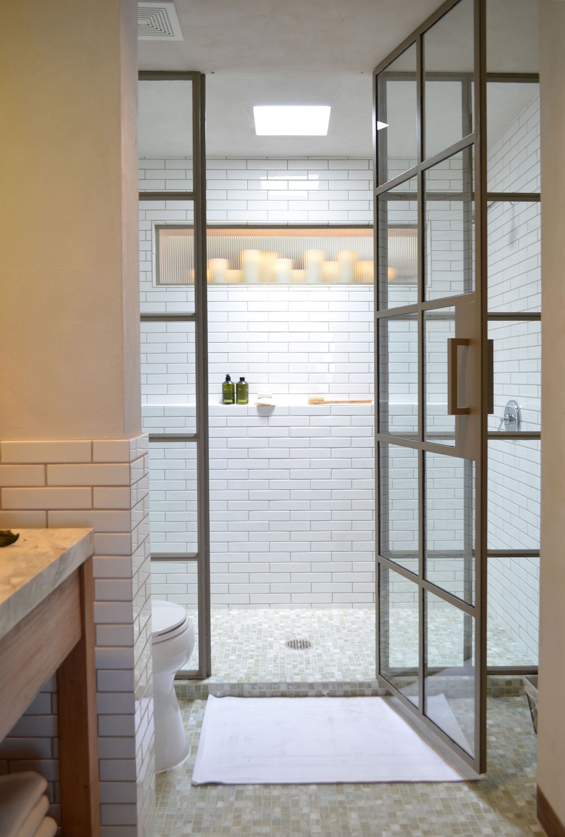 Bathroom with a large glass-paneled shower, white tile, and pebble flooring.