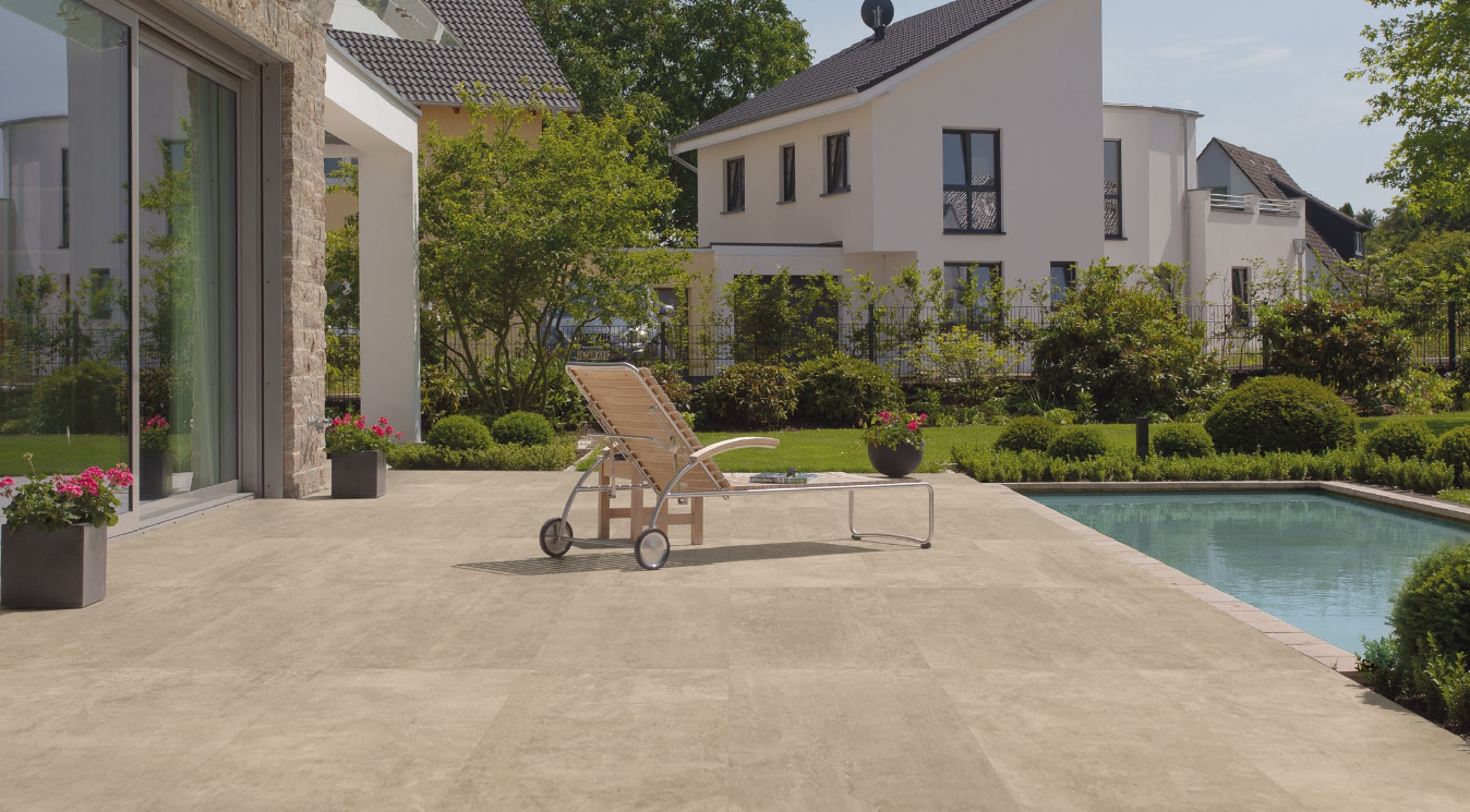 Patio with lounge chair, pool, and home in the background on a sunny day.