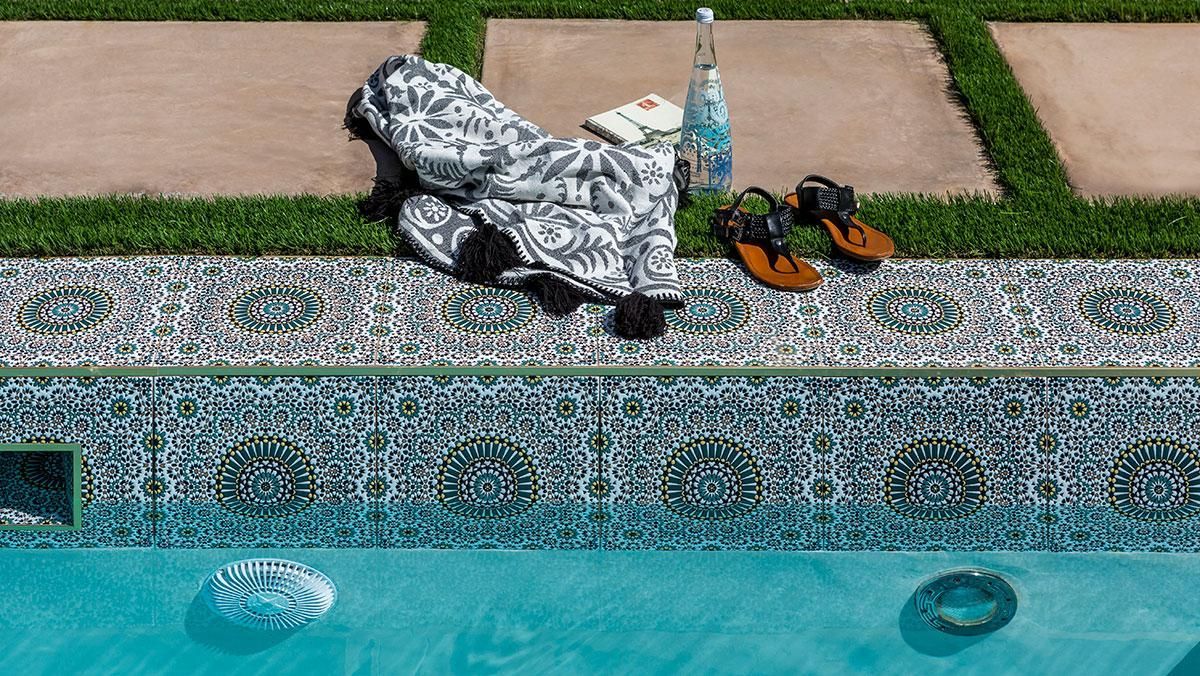 Poolside scene: towel, sandals, bottle of water, book, tile, and turquoise water.