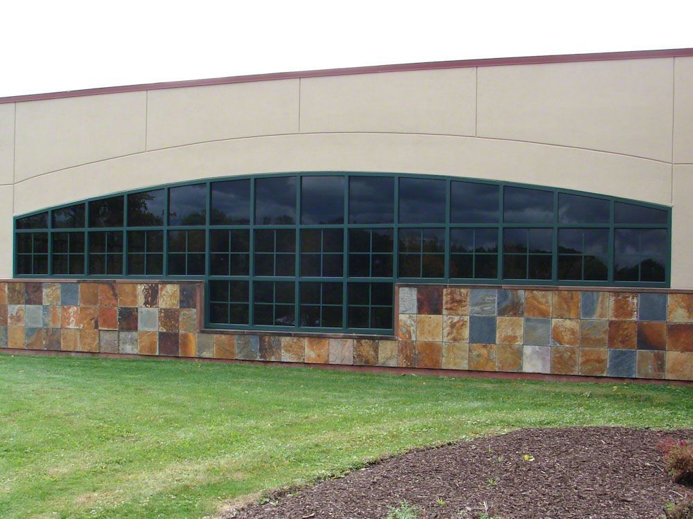 Long, arched window with green grid, above a stone facade on a building, in front of a lawn.