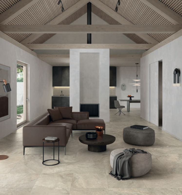 Modern living room with brown leather sectional, stone flooring, and wooden ceiling beams.