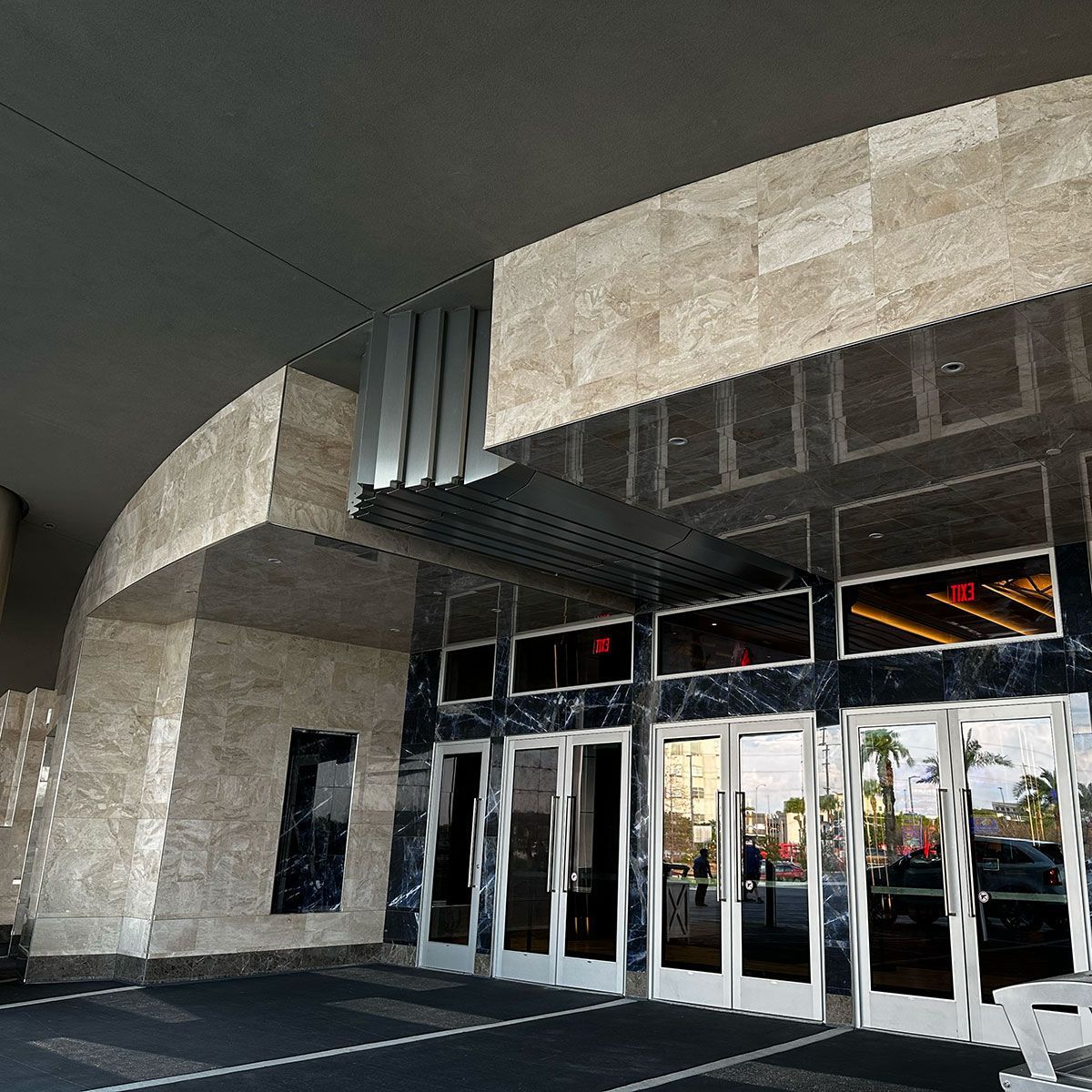 Entrance to a modern building with marble and glass doors. A car is parked outside.