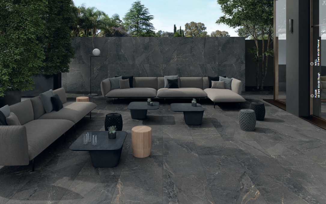 Outdoor patio with gray sectional sofa, dark stone flooring, and low coffee tables.