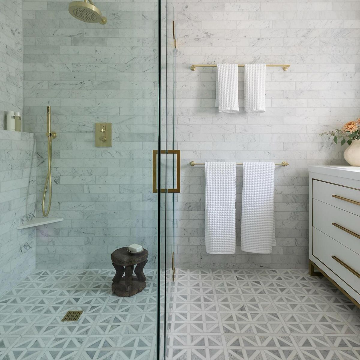Modern bathroom with glass shower, white brick tile, gold fixtures, and decorative geometric floor.