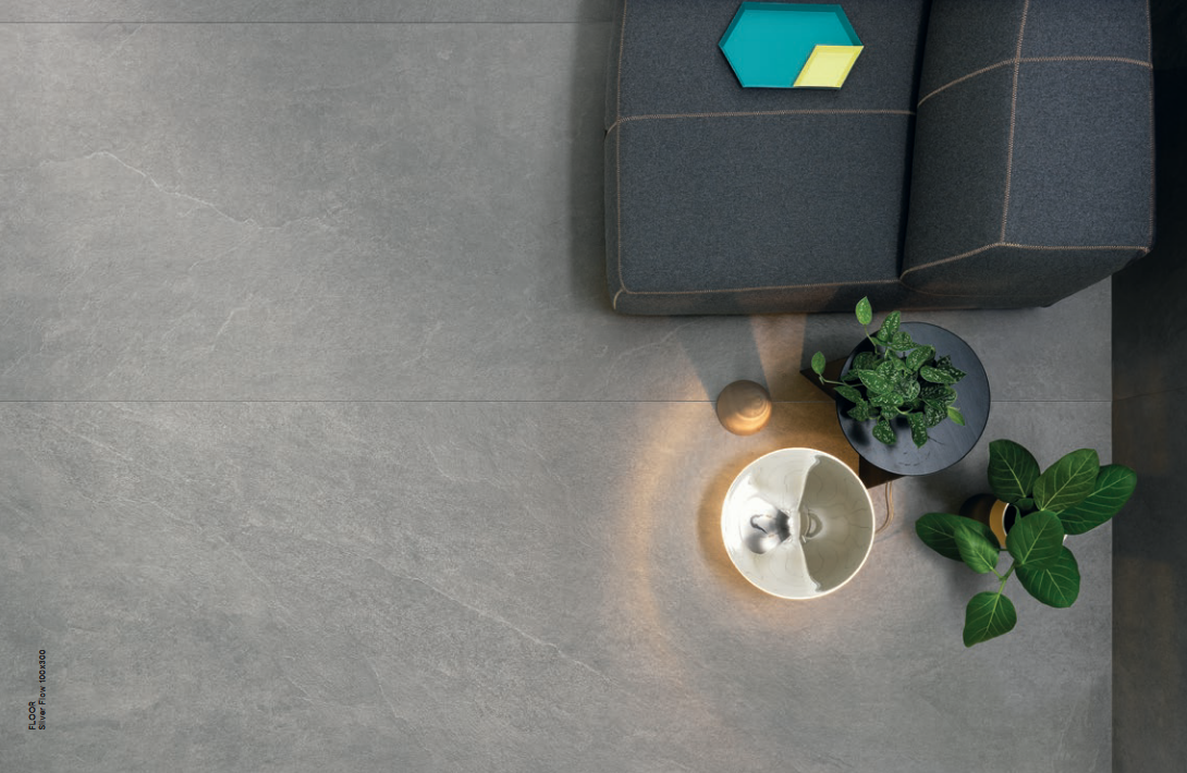 Gray stone floor with modern furniture, plants, and a lamp casting light.