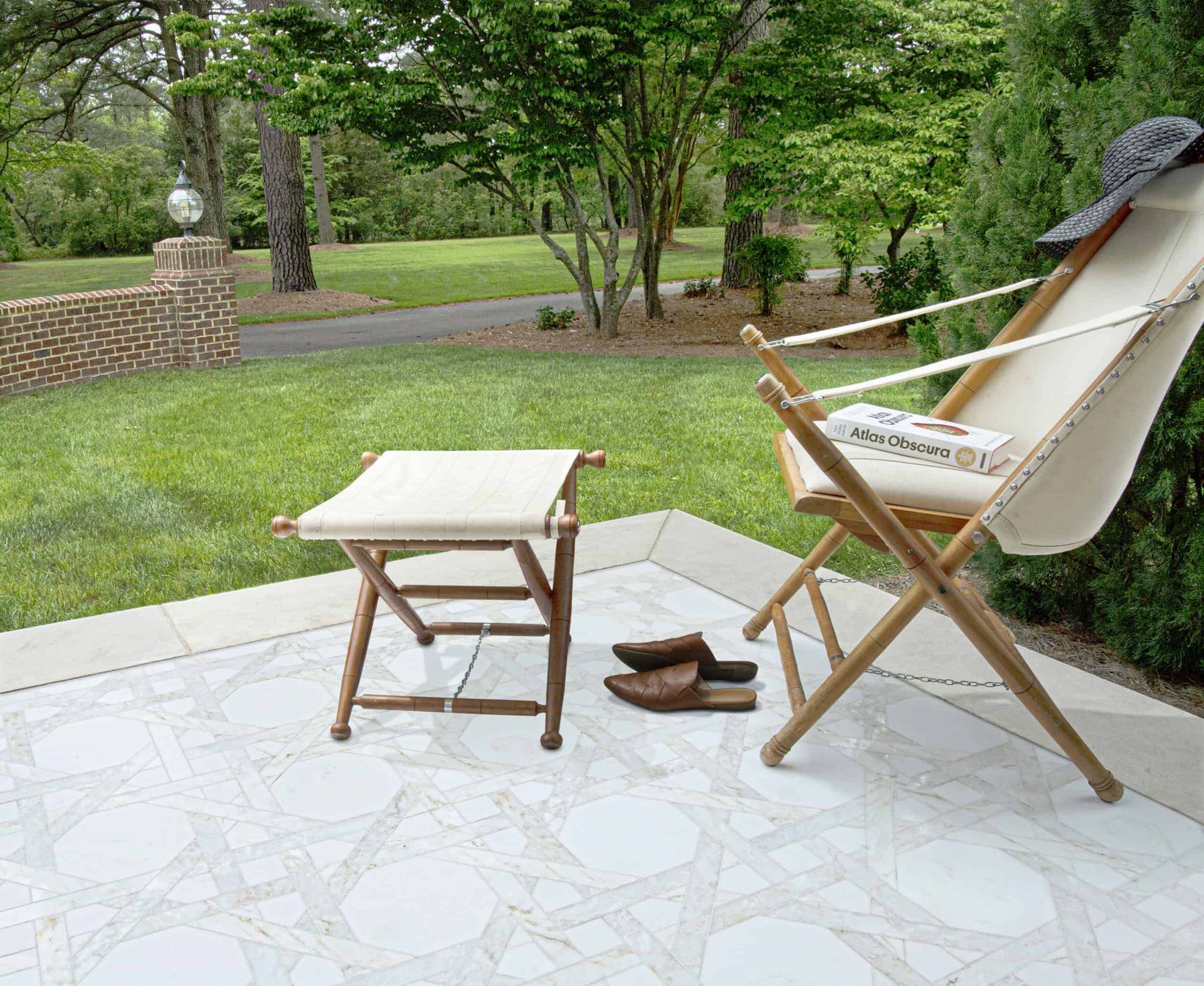 Patio with a white geometric tiled floor, wooden chair, table, shoes, and greenery in the background.