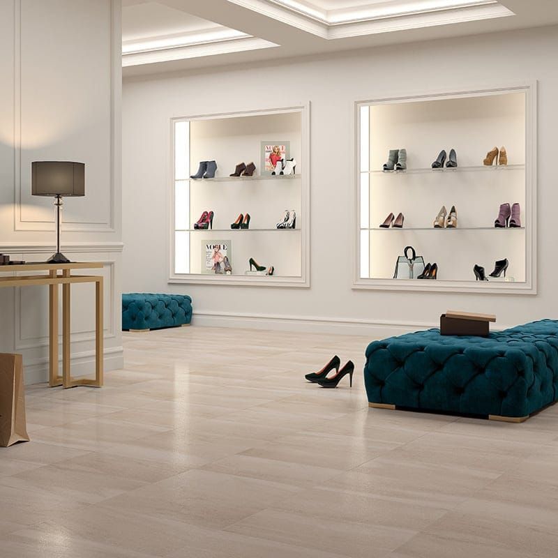 Shoe store interior with display cases, light wood floor, and velvet ottomans. Black heels in the foreground.