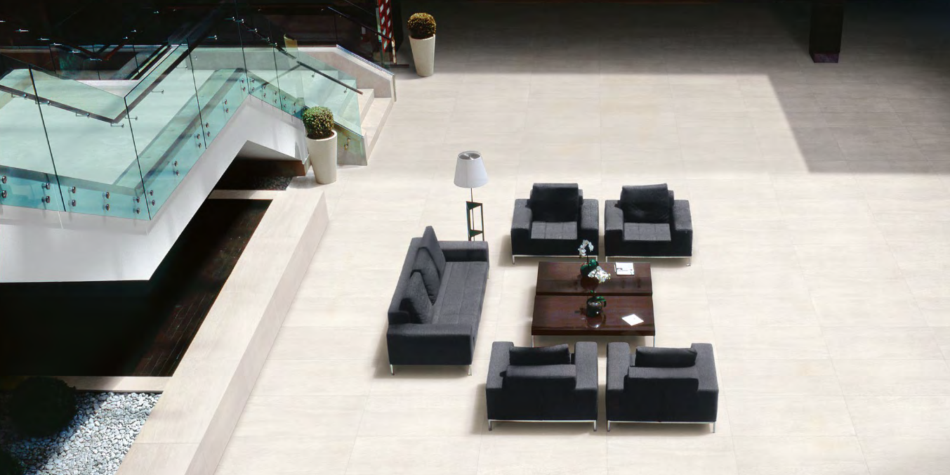 High-angle shot of a modern waiting area with gray sofas, chairs, and a coffee table near a glass staircase.