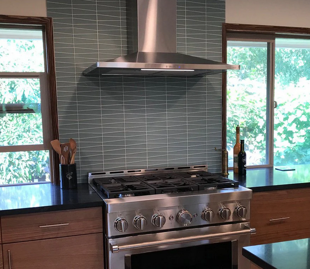 Stainless steel range and hood against blue-tiled backsplash in a modern kitchen.