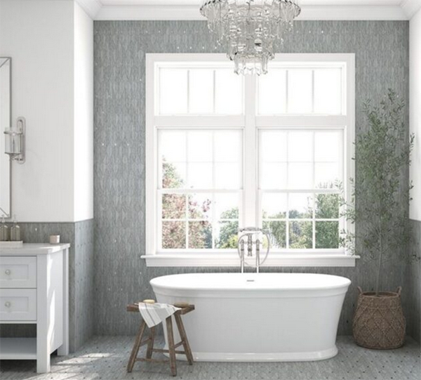 A white bathtub in a bathroom with a window, a chandelier, and a vanity.