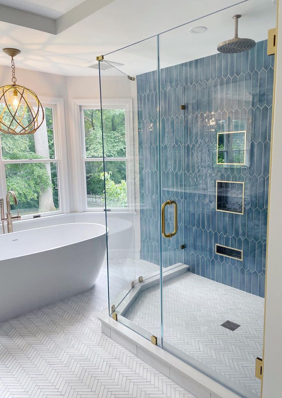 Luxurious bathroom with blue tile shower, freestanding tub, gold fixtures, and natural light.