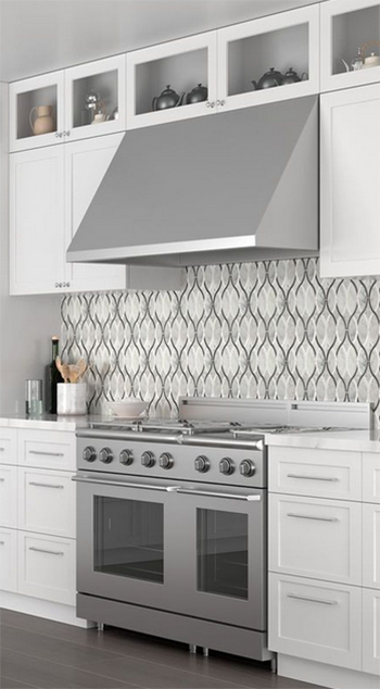 Stainless steel kitchen range and hood, white cabinets, mosaic backsplash.