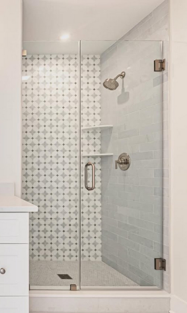 Glass shower door with patterned tile wall, featuring a showerhead and shelves.