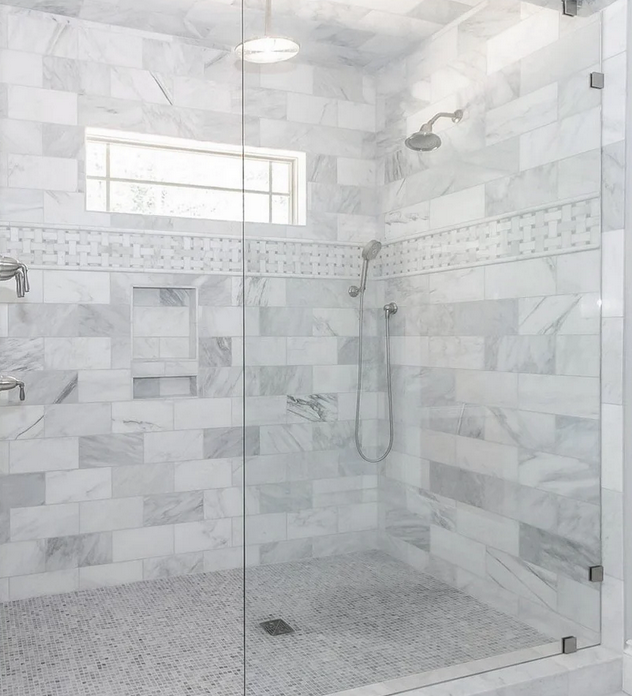 Marble-tiled shower with glass door and window. Features include a shower head and niche.