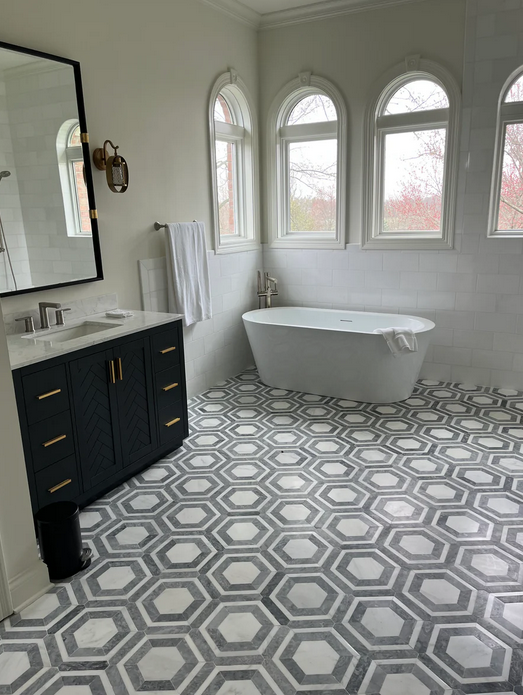 Bathroom with dark blue vanity, white tub, and hexagon tile floor. Three arched windows provide natural light.