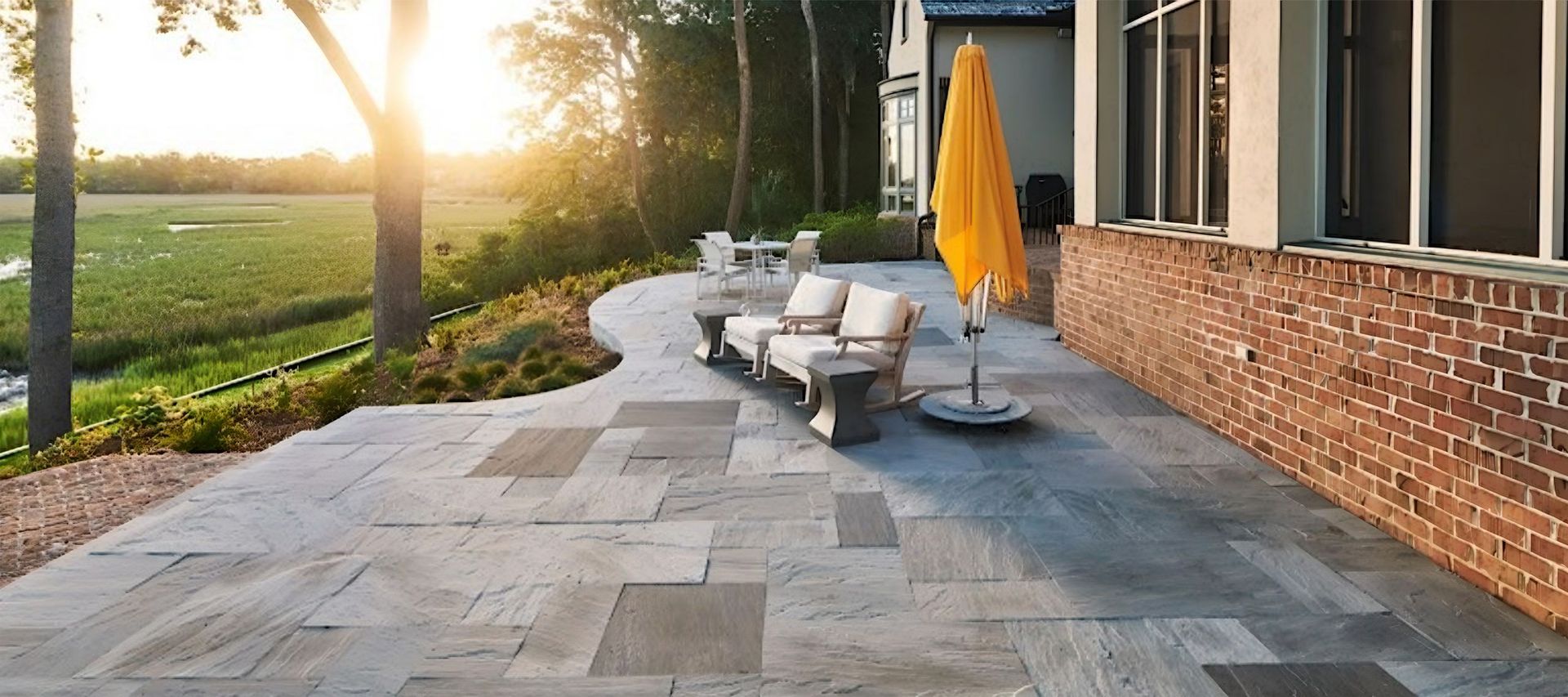 Patio with seating, yellow umbrella, and a view of a field at sunset.