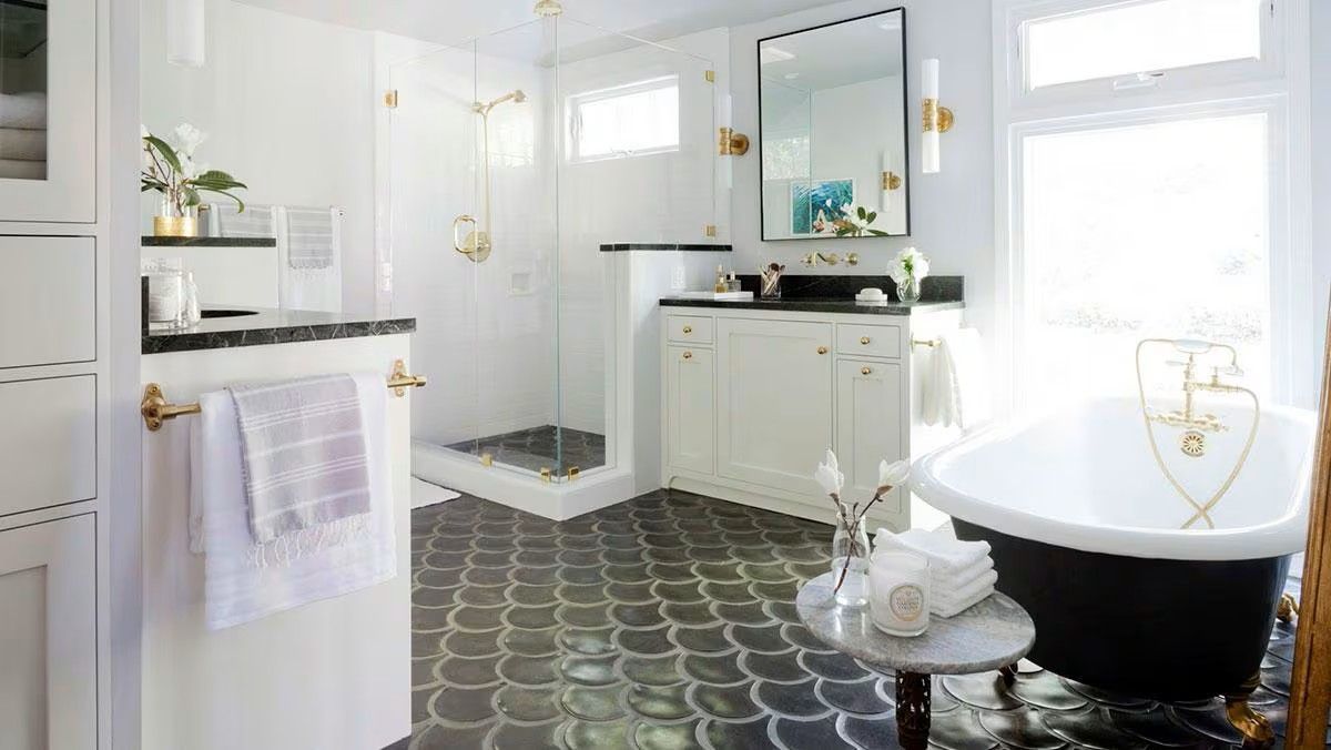 Elegant white bathroom with black and white tile floor, black bathtub, and gold accents.