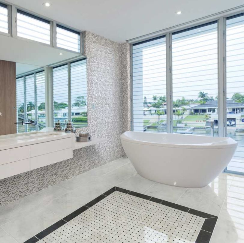 Modern bathroom with a white bathtub, large windows, and mosaic tile accents.