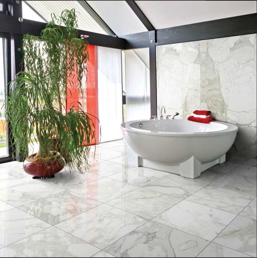 Luxurious bathroom with marble tiles, a white tub, and tall indoor plant.