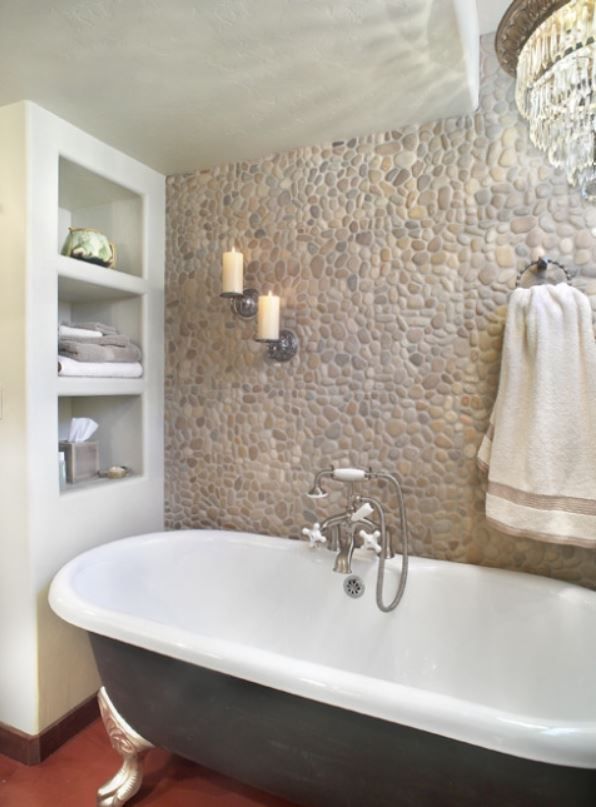 Bathroom with clawfoot tub, pebble tile wall, built-in shelves, candles, and a chandelier.