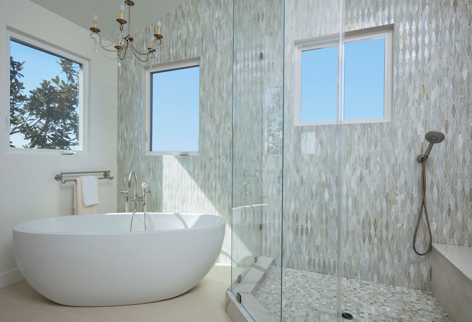 Modern bathroom with a white freestanding tub, glass shower, and textured tile walls.