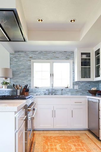 White kitchen with blue tile backsplash, white cabinets, and orange rug.