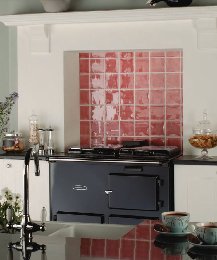 Black range oven with red tiled backsplash, white cabinets, and sink in a kitchen.