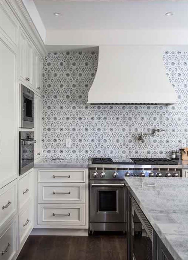 White kitchen with patterned backsplash, stainless steel appliances, and marble countertops.