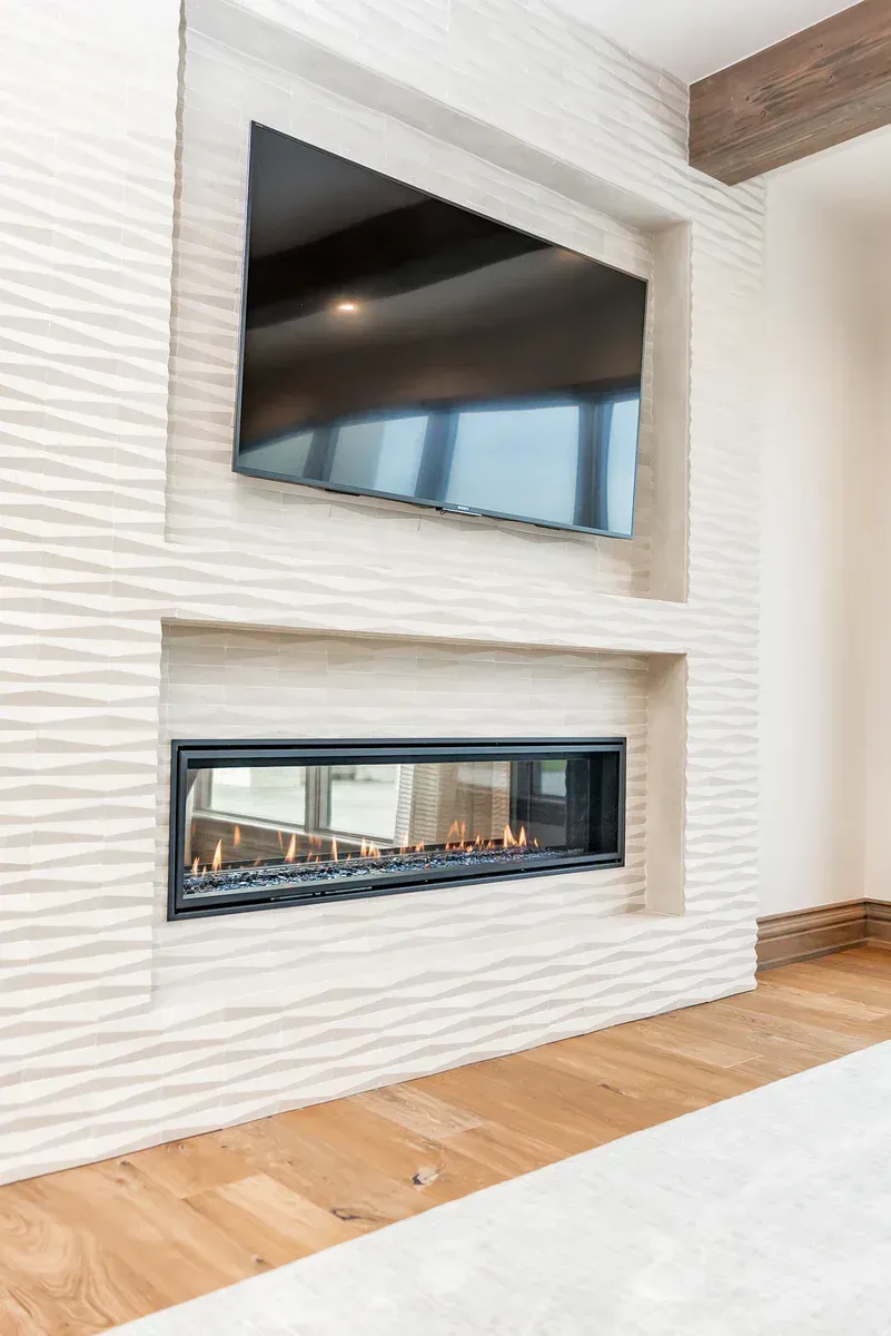 Fireplace and TV built into a light textured wall with wood beams above.