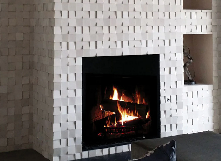 Fireplace with burning logs, set in a white, textured cube-tiled wall with a niche for decor.