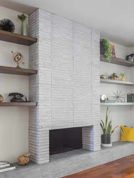 Modern fireplace with brick-like white facade, surrounded by wooden shelves