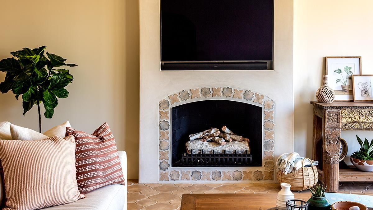 Living room with fireplace, TV, and decorative items. Beige walls, stone fireplace surround.