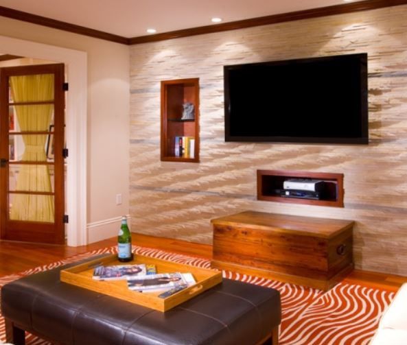 Living room with TV mounted on a textured wall, wooden accents, and a leather ottoman.