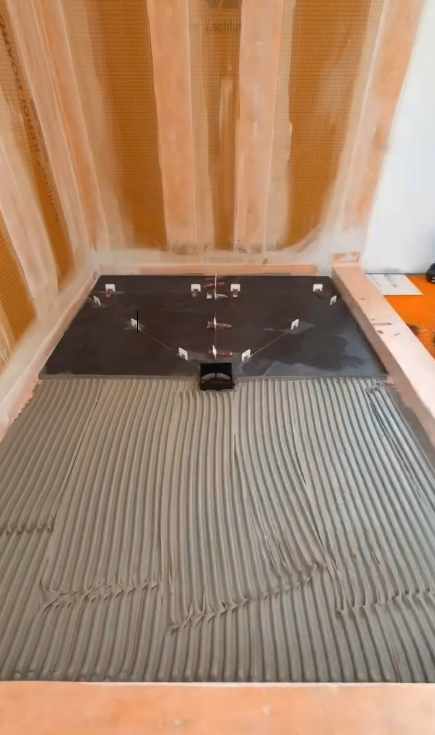 Shower base being tiled, with wet mortar applied in parallel lines.