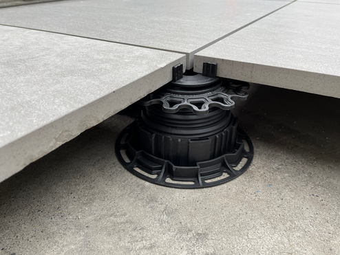 Gray patio tiles supported by black adjustable pedestals on concrete.