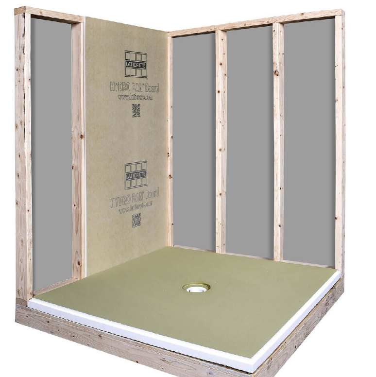 Shower stall under construction, green base with drain, tan wall panels on wood frame.