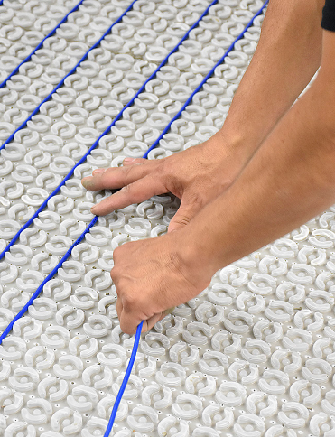 Person installing blue tubing into a white floor heating system.