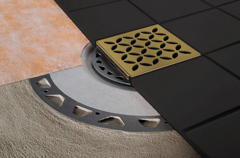 Close-up of a shower drain with black tile and gold-colored grate.