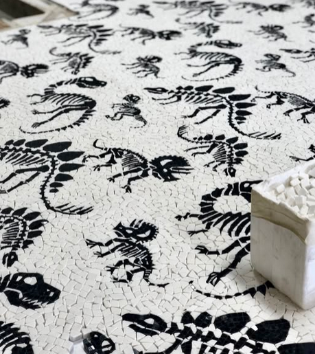 White mosaic featuring black dinosaur skeleton patterns, with a stack of white tiles in the foreground.