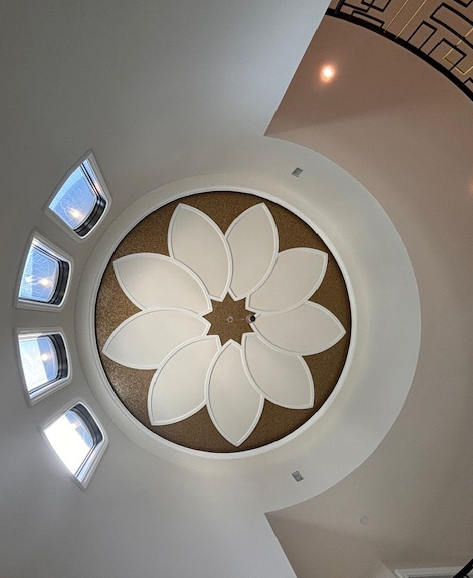 Looking up at a ceiling dome with a flower design in gold and white, with small arched windows.