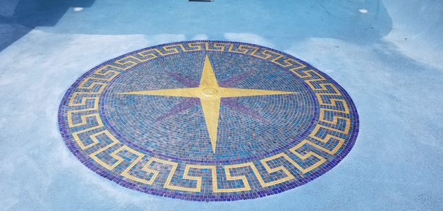 Circular mosaic on a blue surface, with a yellow compass rose design and a Greek key border.