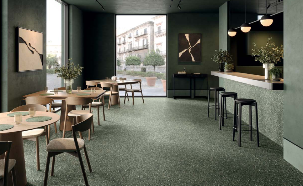 Interior of a modern, green-toned cafe with round tables, chairs, a bar, and a large window with a city view.