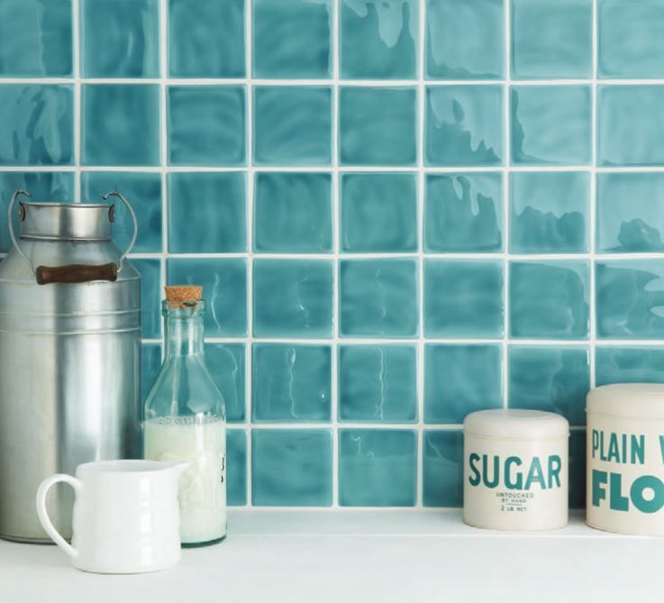 Teal square tiles backsplash behind kitchen counter with sugar and flour canisters, milk bottles and pitcher.