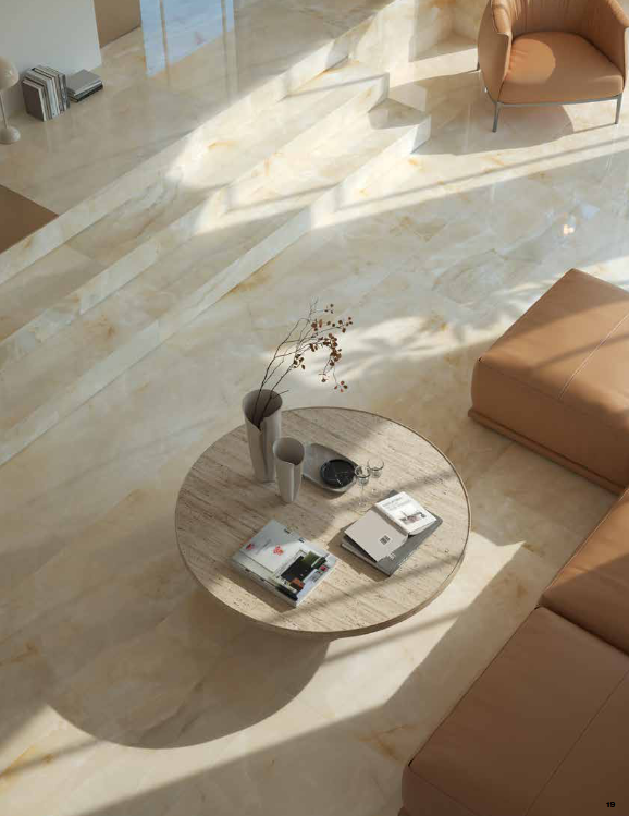 Living room with marble floors, circular coffee table, and tan leather furniture. Sunlight streams through a window.