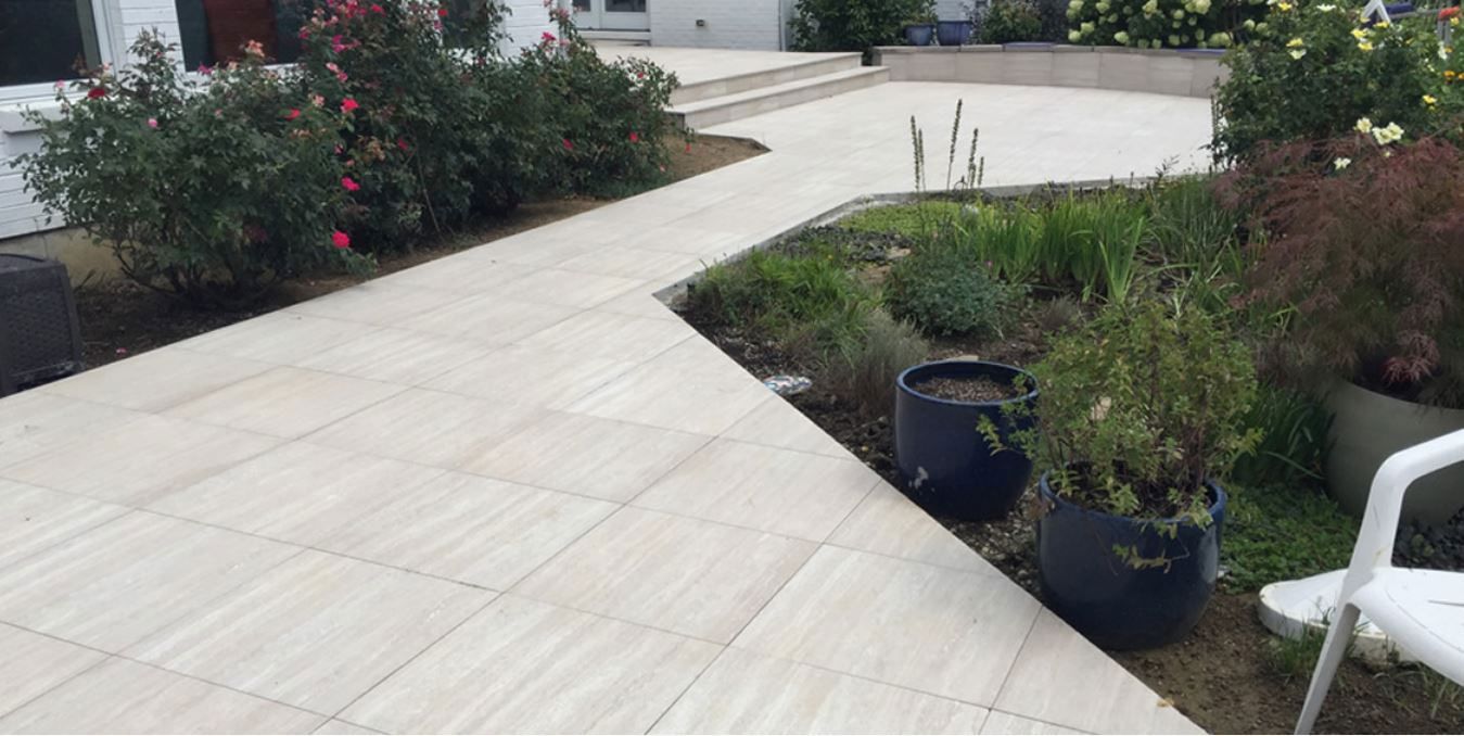 Pathway of light-colored tiles leading to an outdoor garden area. Potted plants and bushes line the path.