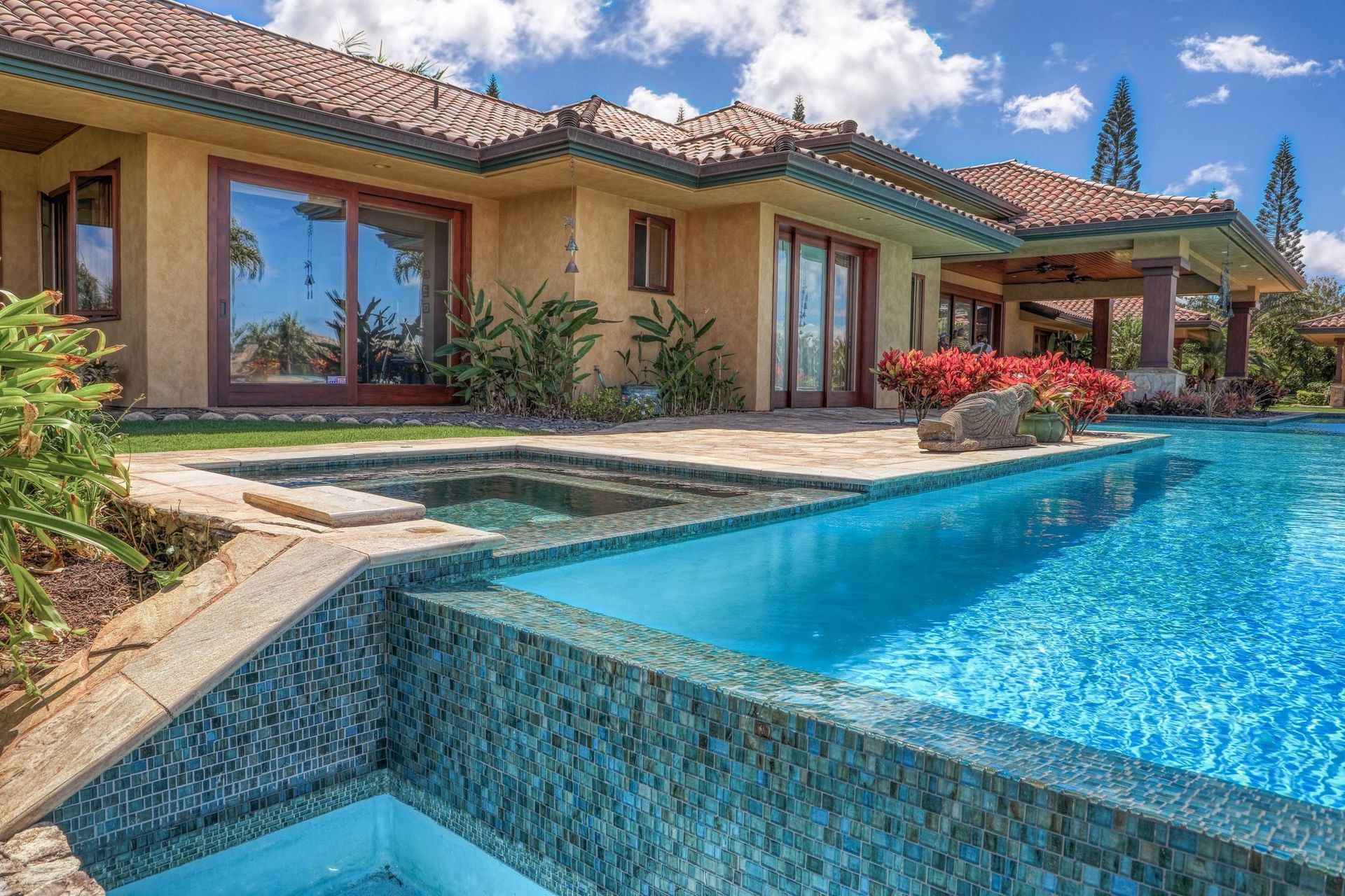 Luxurious home with pool and spa; blue water, terracotta roof, lush greenery.