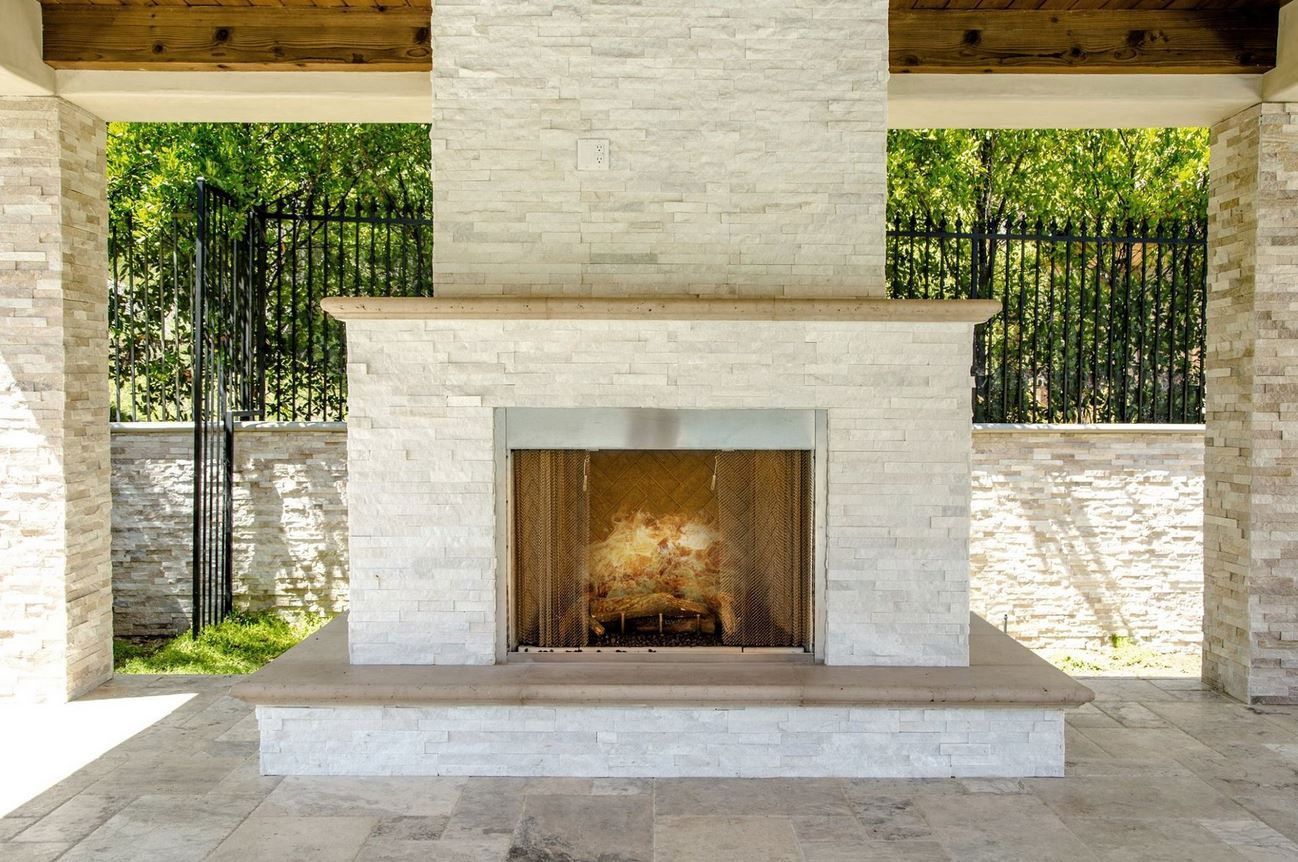 Outdoor stone fireplace with burning flames, surrounded by columns and a patio.